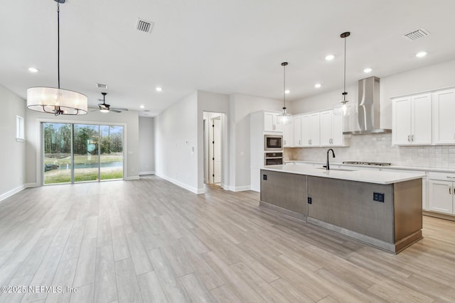 kitchen with white cabinets, stainless steel appliances, an island with sink, and wall chimney range hood