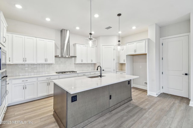 kitchen with an island with sink, sink, wall chimney range hood, and decorative light fixtures