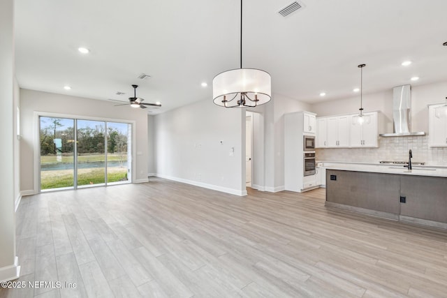 interior space featuring white cabinets, hanging light fixtures, wall chimney exhaust hood, and appliances with stainless steel finishes