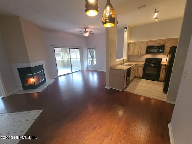 kitchen with ceiling fan, black appliances, a tiled fireplace, pendant lighting, and sink