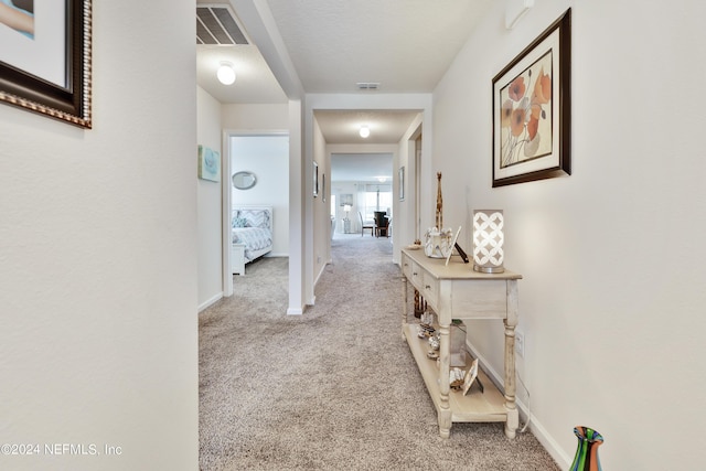 corridor with light carpet, visible vents, and baseboards