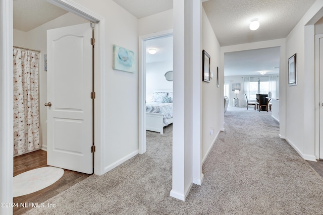 corridor featuring a textured ceiling, baseboards, and carpet flooring