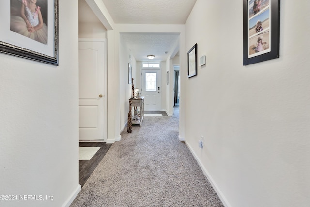 hall with carpet floors, baseboards, and a textured ceiling