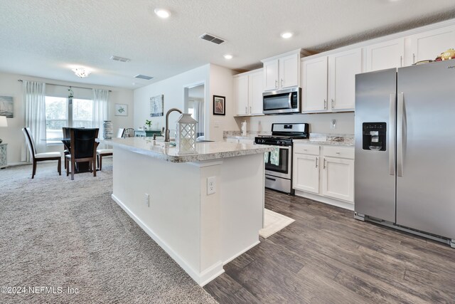 kitchen featuring stainless steel appliances, a center island with sink, a textured ceiling, white cabinets, and dark carpet