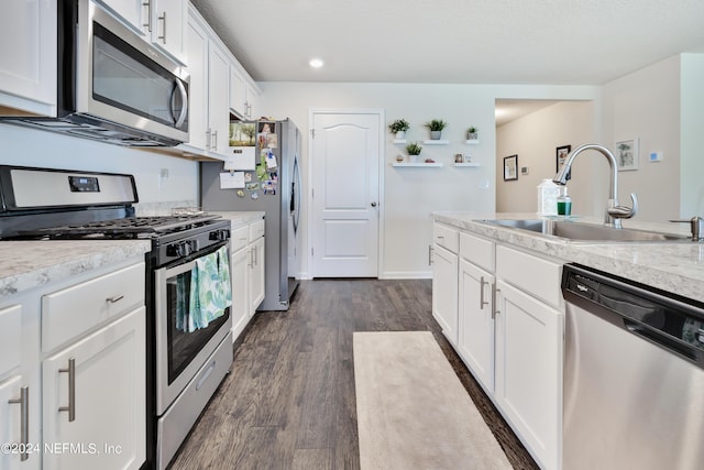 kitchen featuring dark wood-style floors, stainless steel appliances, white cabinets, a sink, and baseboards