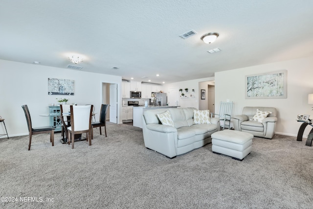 living room featuring baseboards, visible vents, a textured ceiling, and light colored carpet