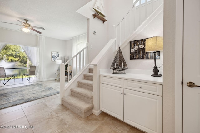 stairway with ceiling fan, a textured ceiling, baseboards, and tile patterned floors