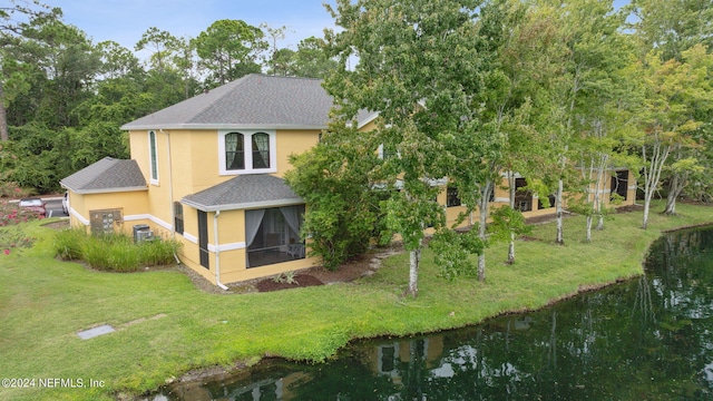 exterior space with a shingled roof, a sunroom, a water view, and stucco siding