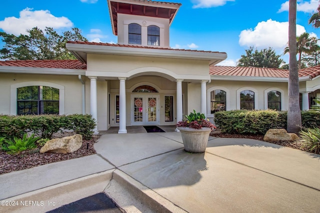 property entrance with a tiled roof, french doors, and stucco siding