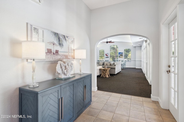 hall with light tile patterned floors, baseboards, arched walkways, and light colored carpet