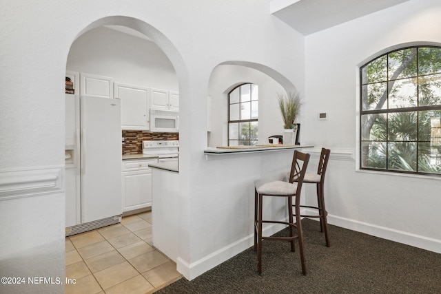 kitchen with light tile patterned floors, white appliances, baseboards, white cabinets, and backsplash