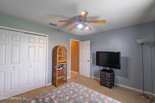 carpeted bedroom with a textured ceiling, ceiling fan, and a closet