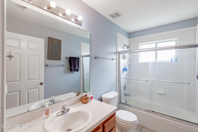 full bathroom featuring vanity, a textured ceiling, shower / bath combination with glass door, toilet, and tile patterned floors