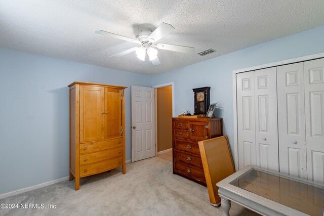 bedroom with a closet, ceiling fan, light colored carpet, and a textured ceiling