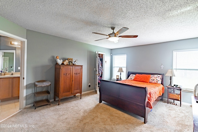 bedroom with a closet, a textured ceiling, light colored carpet, ensuite bath, and ceiling fan