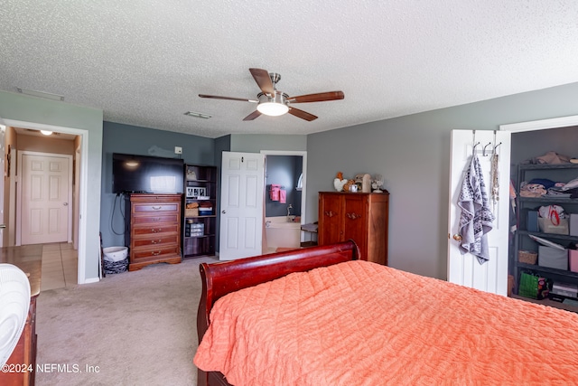 carpeted bedroom with a textured ceiling, connected bathroom, and ceiling fan