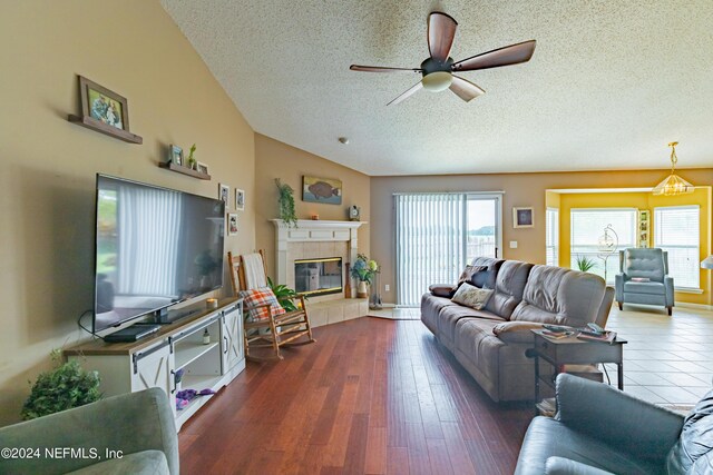 living room featuring a textured ceiling, a tile fireplace, ceiling fan with notable chandelier, and dark wood-type flooring