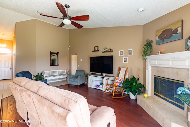 living room featuring a textured ceiling, a tile fireplace, vaulted ceiling, dark hardwood / wood-style flooring, and ceiling fan