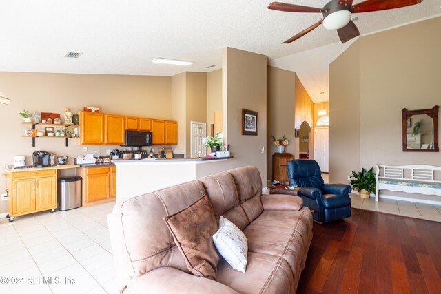 living room with light hardwood / wood-style floors, a textured ceiling, lofted ceiling, and ceiling fan