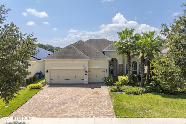 view of front of property featuring a garage, roof with shingles, decorative driveway, a front lawn, and stucco siding