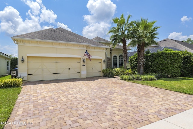 view of front of house with decorative driveway, roof with shingles, an attached garage, and stucco siding