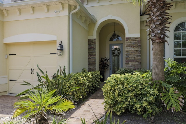 entrance to property featuring an attached garage, stone siding, and stucco siding