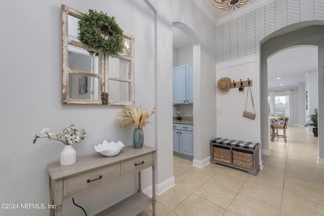 corridor featuring arched walkways, light tile patterned flooring, crown molding, and baseboards