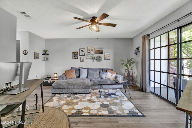 living room with ceiling fan, a textured ceiling, and light hardwood / wood-style floors