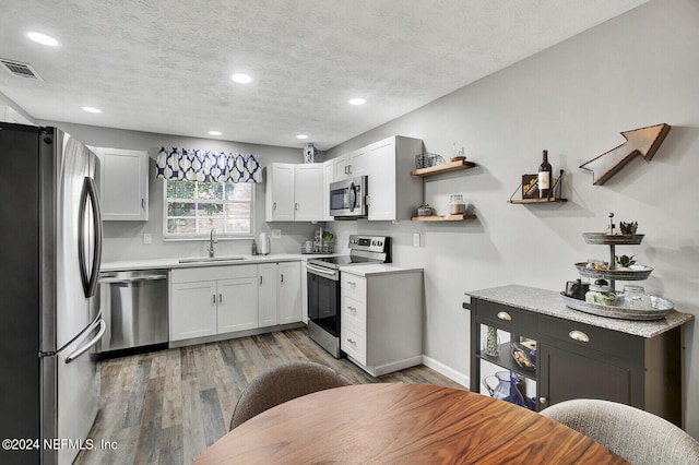 kitchen featuring appliances with stainless steel finishes, a textured ceiling, wood-type flooring, and sink