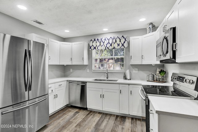 kitchen featuring appliances with stainless steel finishes, light hardwood / wood-style floors, white cabinetry, and sink