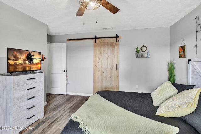 bedroom with ceiling fan, a barn door, wood-type flooring, and a textured ceiling