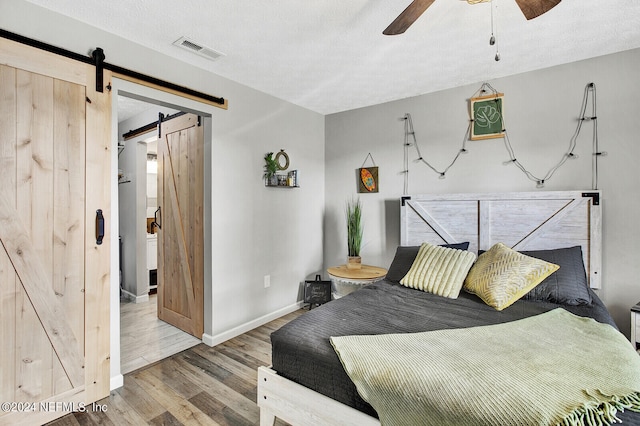 bedroom featuring a textured ceiling, ceiling fan, hardwood / wood-style floors, and a barn door