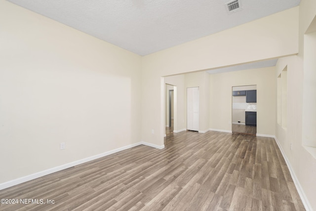 unfurnished room with visible vents, a textured ceiling, baseboards, and wood finished floors