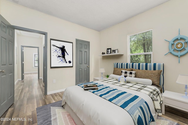 bedroom with a textured ceiling, wood finished floors, and baseboards