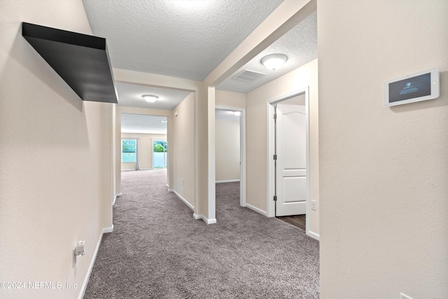 hallway with baseboards, visible vents, carpet flooring, and a textured ceiling
