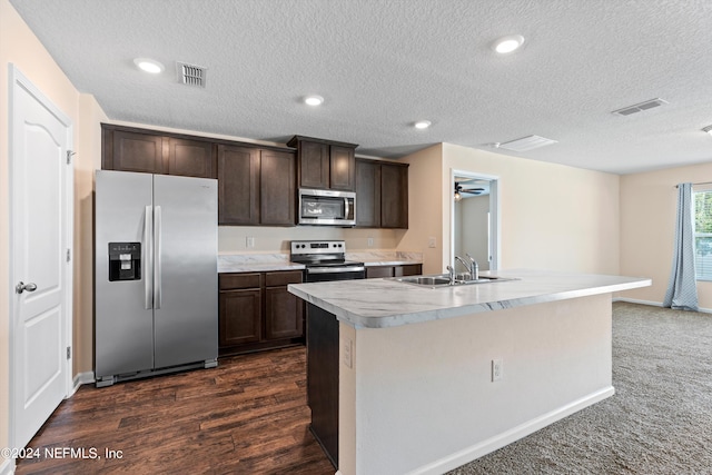 kitchen with dark carpet, stainless steel appliances, a textured ceiling, and an island with sink