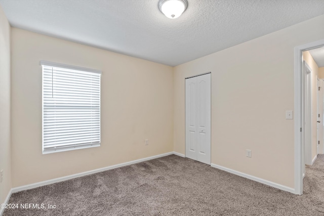 unfurnished bedroom featuring a textured ceiling, carpet floors, and a closet