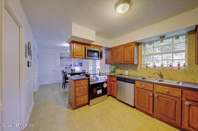 kitchen featuring brown cabinetry, dark countertops, appliances with stainless steel finishes, a peninsula, and a sink