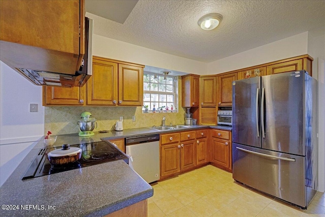 kitchen featuring brown cabinets, backsplash, freestanding refrigerator, a sink, and dishwashing machine