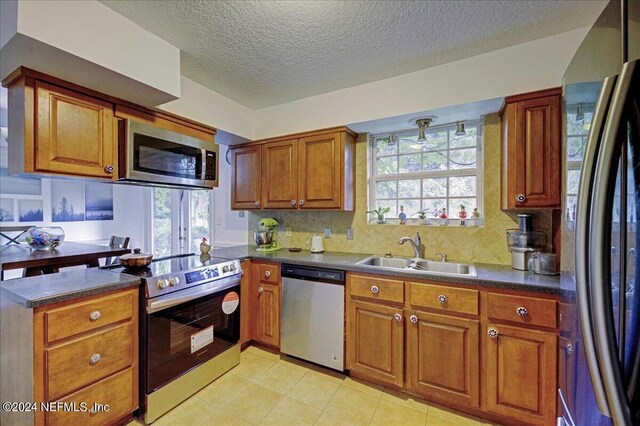 kitchen featuring a peninsula, a sink, appliances with stainless steel finishes, brown cabinetry, and dark countertops