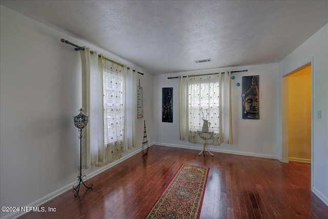 interior space featuring a textured ceiling, hardwood / wood-style floors, visible vents, and baseboards