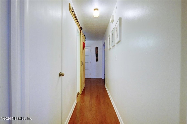 hallway with dark wood-style floors, a barn door, and baseboards