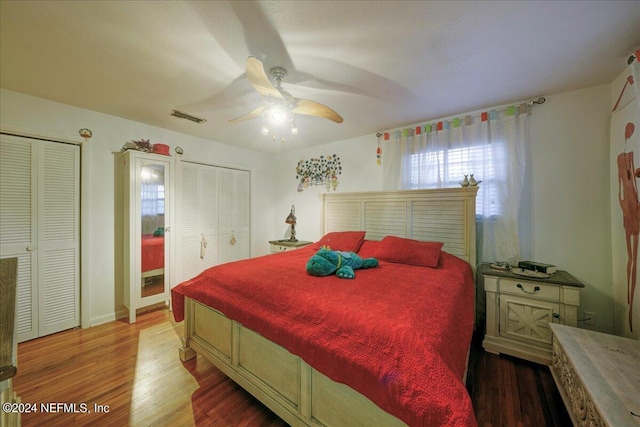 bedroom with wood finished floors, visible vents, ceiling fan, and two closets