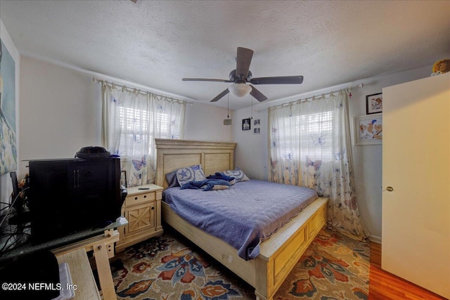 bedroom featuring light wood-style floors, ceiling fan, multiple windows, and a textured ceiling