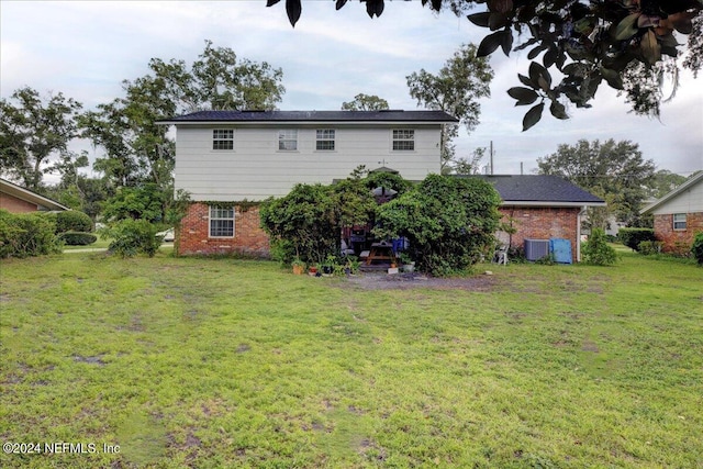 rear view of property featuring cooling unit, brick siding, and a lawn