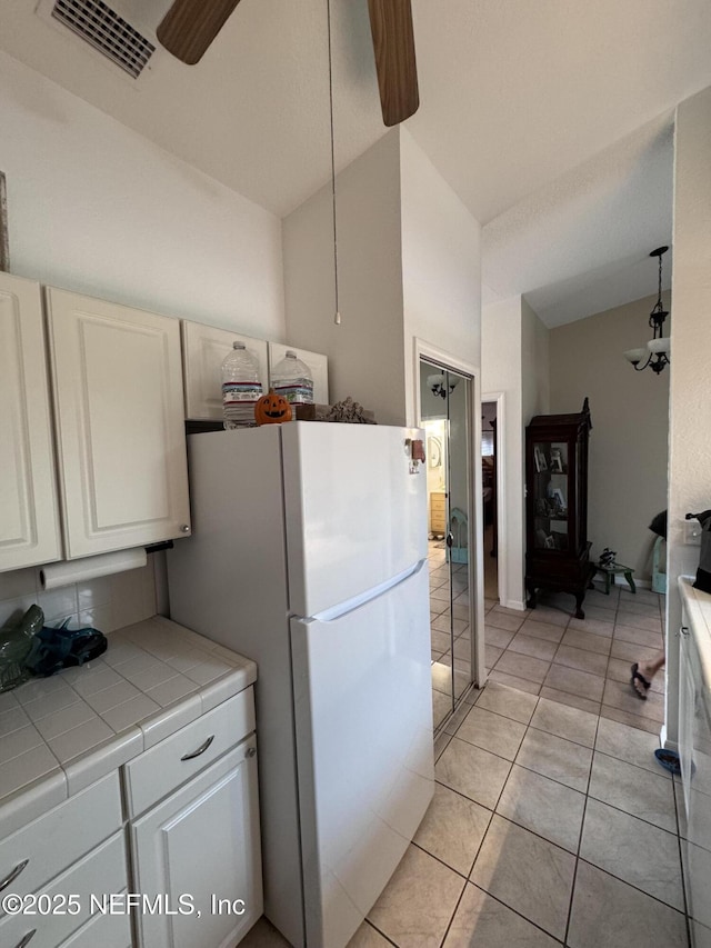 kitchen featuring freestanding refrigerator, white cabinets, visible vents, ceiling fan, and tile countertops