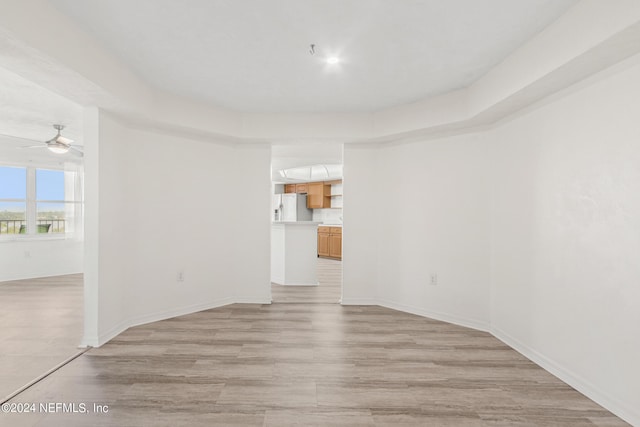 empty room with ceiling fan, light wood finished floors, and baseboards