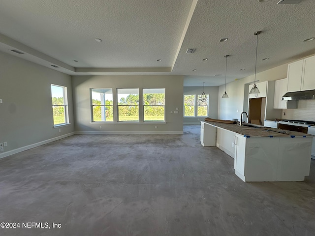 kitchen with white cabinetry, hanging light fixtures, backsplash, a textured ceiling, and a kitchen island with sink