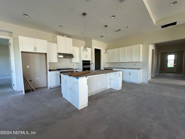 kitchen with white cabinets, a textured ceiling, backsplash, and an island with sink