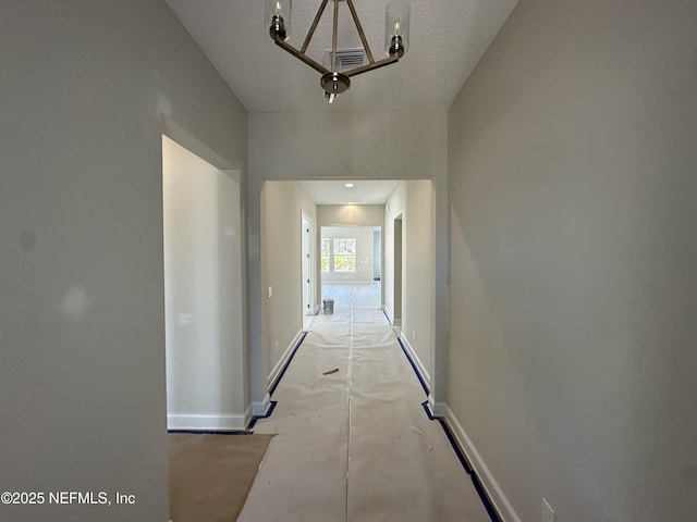 corridor featuring visible vents, a textured ceiling, and baseboards